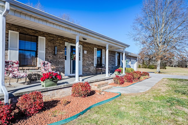 view of exterior entry featuring covered porch, a lawn, and a garage