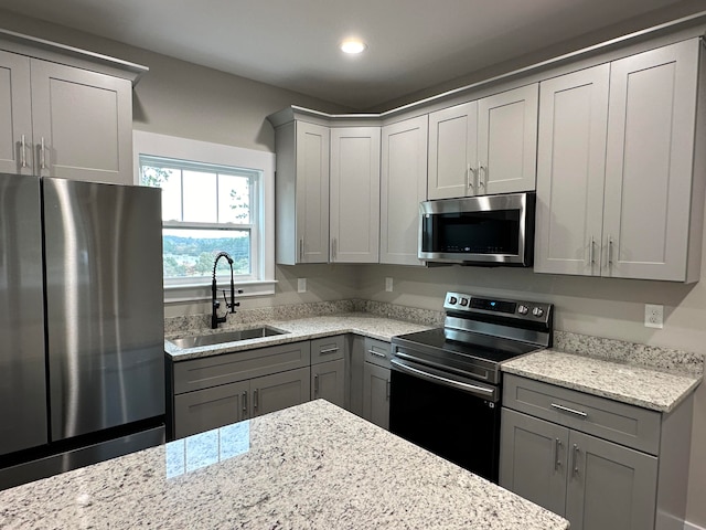 kitchen with stainless steel appliances, light stone counters, gray cabinetry, and sink