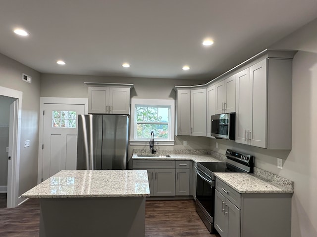 kitchen with light stone counters, gray cabinetry, stainless steel appliances, sink, and a center island