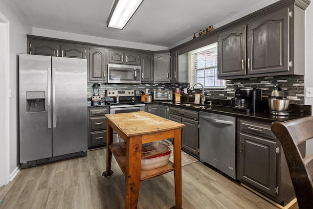 kitchen featuring stainless steel appliances, dark countertops, a sink, and light wood-style flooring