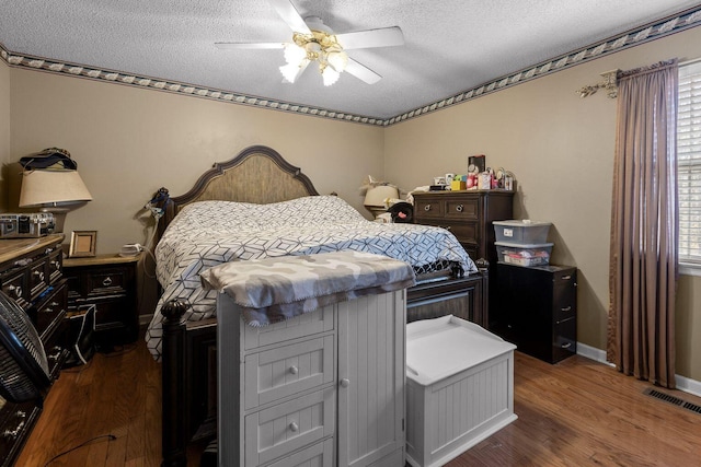 bedroom featuring baseboards, visible vents, a ceiling fan, dark wood finished floors, and a textured ceiling