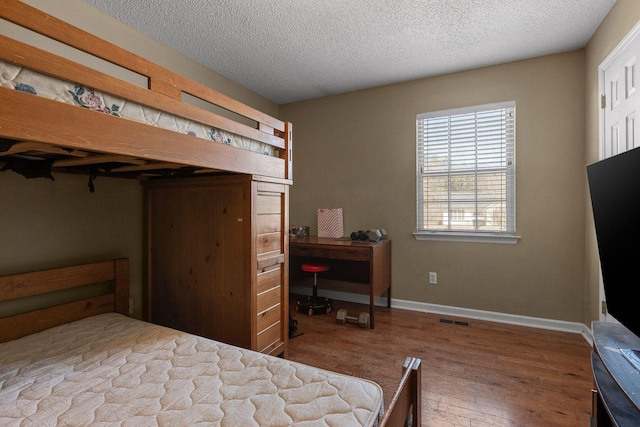 bedroom featuring visible vents, a textured ceiling, baseboards, and wood finished floors