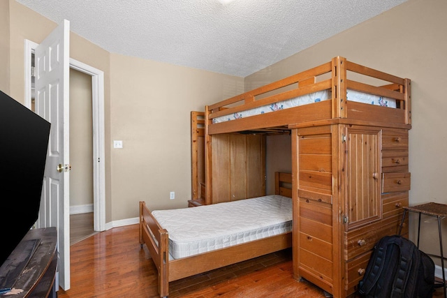 bedroom with dark wood-style floors, a textured ceiling, and baseboards