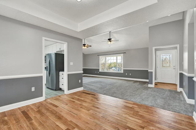 unfurnished living room with a textured ceiling, a raised ceiling, ceiling fan, and light hardwood / wood-style floors