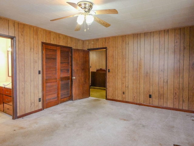 unfurnished bedroom with ceiling fan, light colored carpet, ensuite bathroom, and wooden walls