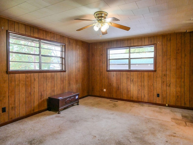 carpeted empty room with ceiling fan and wood walls