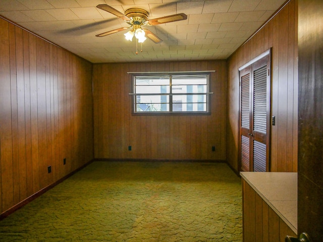 carpeted empty room featuring wood walls and ceiling fan