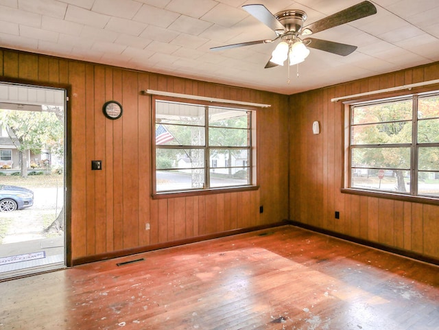 unfurnished room with hardwood / wood-style flooring, plenty of natural light, wooden walls, and ceiling fan