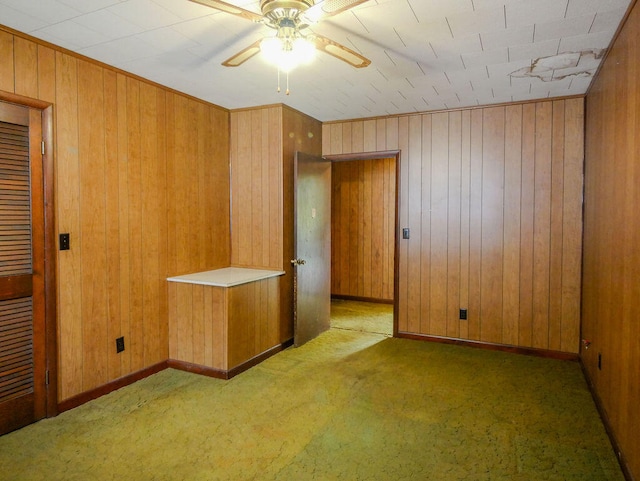 empty room featuring dark colored carpet, ceiling fan, and wooden walls