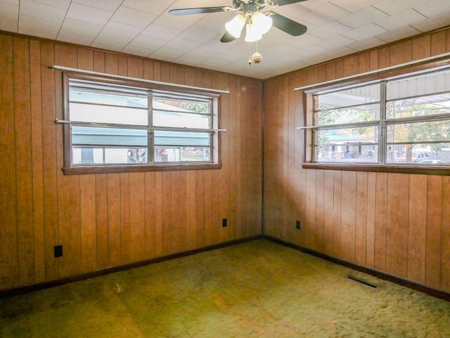 spare room featuring wooden walls, ceiling fan, and dark carpet