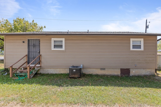 rear view of house featuring central AC unit and a lawn