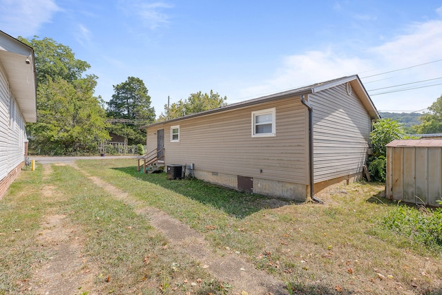 view of side of property with a lawn, central AC unit, and a storage shed