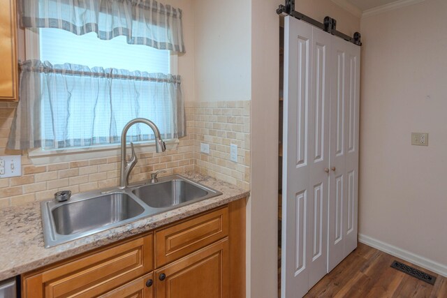 kitchen featuring decorative backsplash, light stone counters, ornamental molding, dark wood-type flooring, and sink