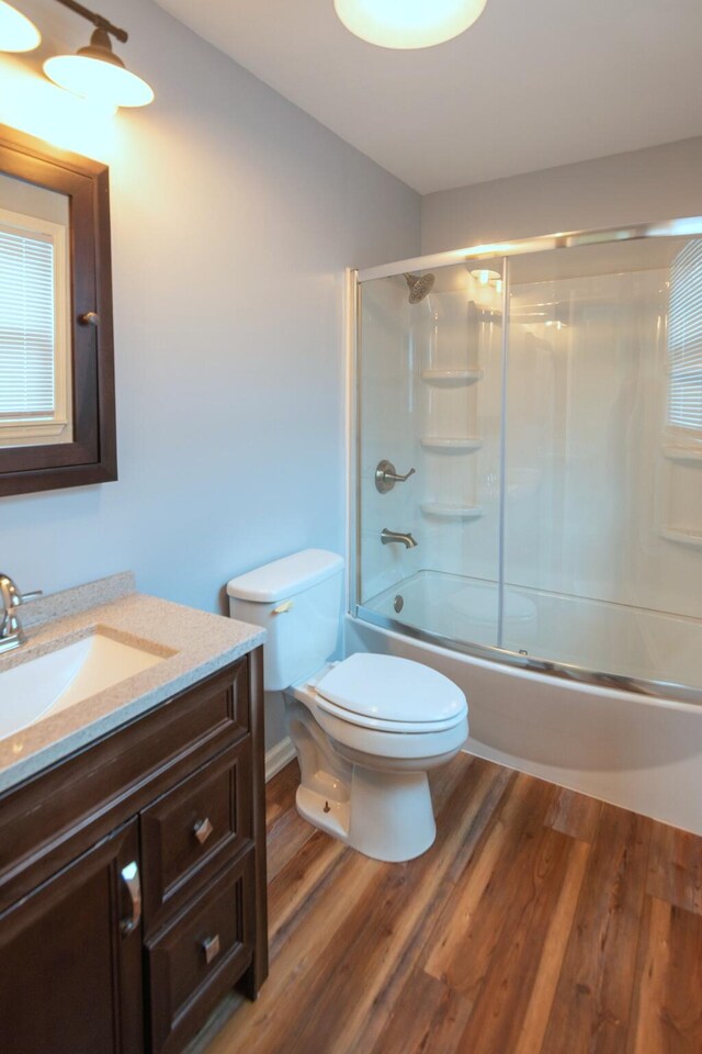 full bathroom featuring shower / bath combination with glass door, hardwood / wood-style floors, vanity, and toilet