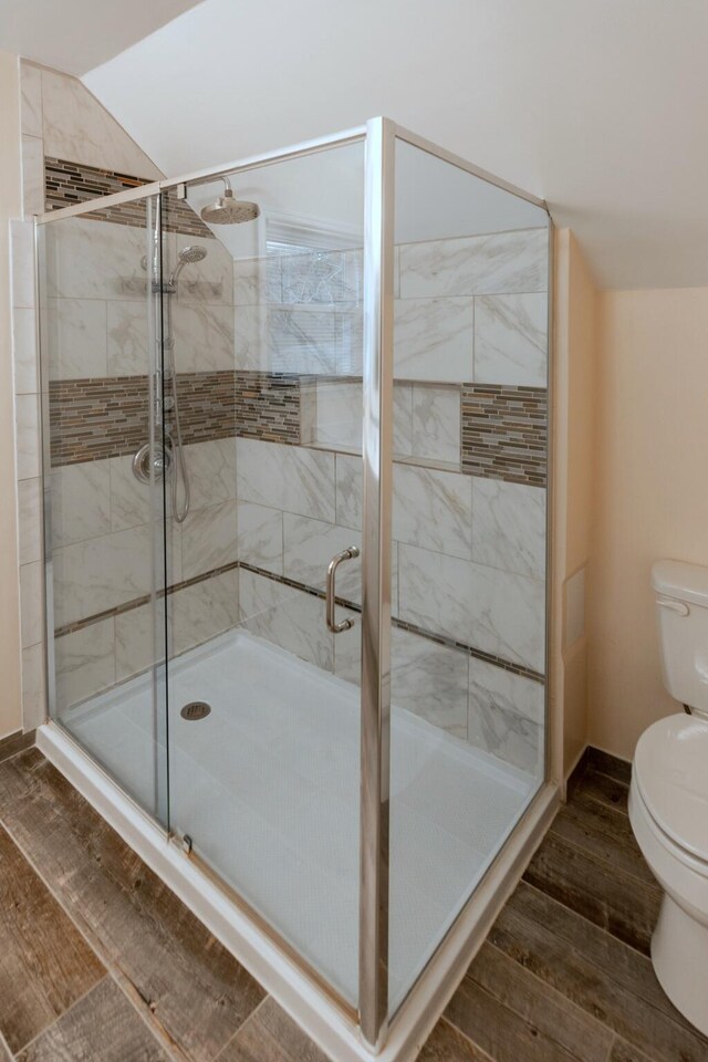 bathroom with vaulted ceiling, hardwood / wood-style flooring, toilet, and a shower with shower door