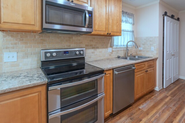 kitchen featuring sink, a barn door, ornamental molding, wood-type flooring, and stainless steel appliances