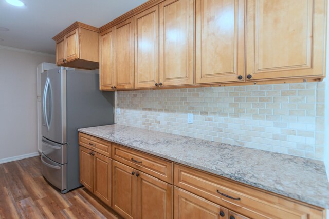 kitchen with dark hardwood / wood-style flooring, backsplash, light stone counters, crown molding, and stainless steel refrigerator