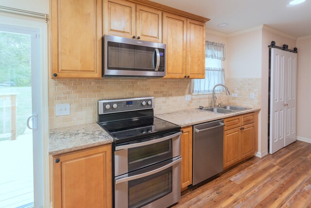 kitchen featuring sink, stainless steel appliances, a barn door, crown molding, and light wood-type flooring