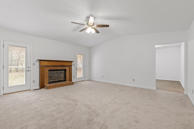 unfurnished living room featuring vaulted ceiling, light colored carpet, ceiling fan, a brick fireplace, and a textured ceiling