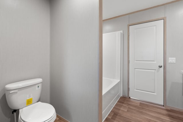 bathroom with a tub to relax in, hardwood / wood-style floors, and toilet