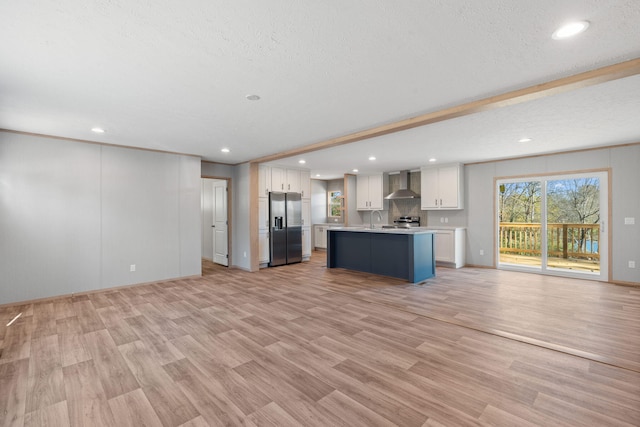 kitchen with white cabinetry, a center island, wall chimney exhaust hood, stainless steel appliances, and light hardwood / wood-style floors