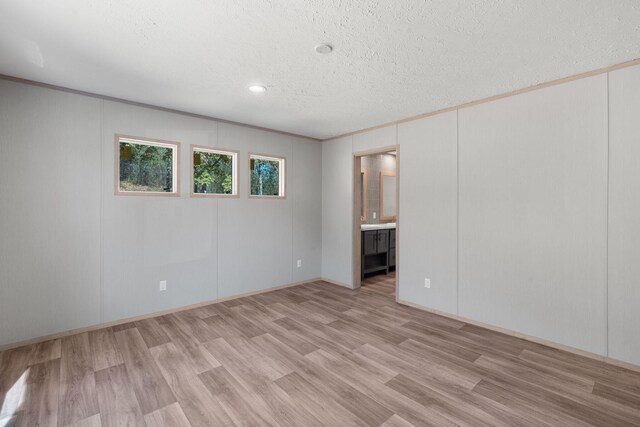 unfurnished room featuring a textured ceiling, light hardwood / wood-style floors, and crown molding