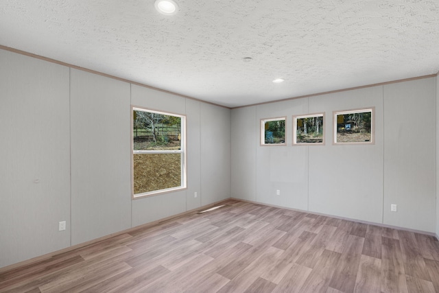 empty room with a textured ceiling, light hardwood / wood-style flooring, and crown molding