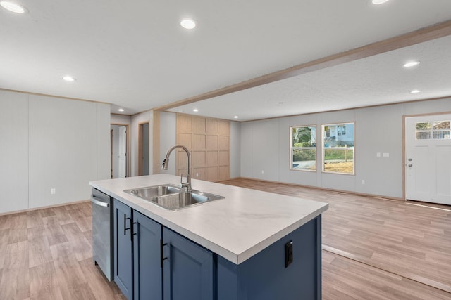 kitchen featuring a center island with sink, sink, stainless steel dishwasher, blue cabinetry, and light hardwood / wood-style floors