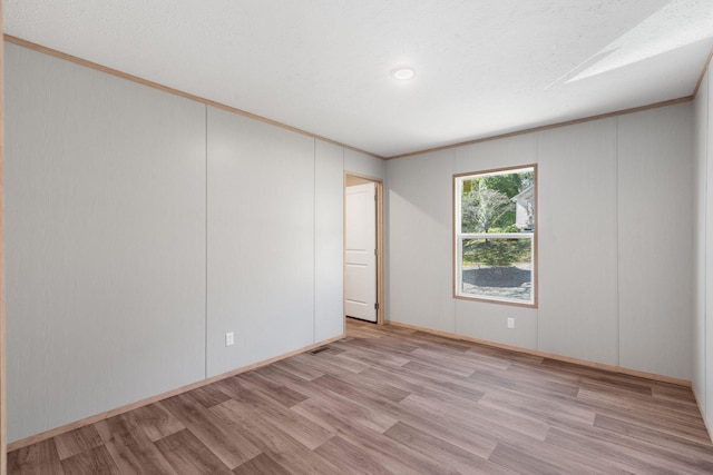 empty room featuring crown molding, light wood-type flooring, and a textured ceiling