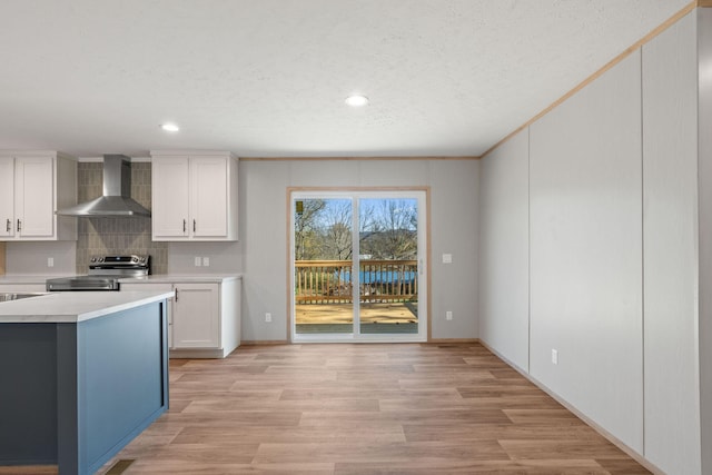 kitchen with tasteful backsplash, stainless steel electric stove, wall chimney range hood, light hardwood / wood-style floors, and white cabinetry