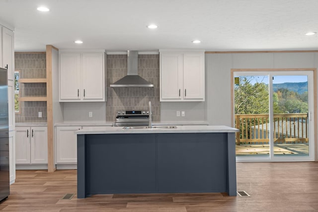 kitchen with sink, wall chimney exhaust hood, stainless steel stove, light hardwood / wood-style floors, and white cabinets