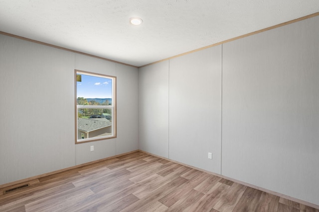 empty room featuring ornamental molding, a textured ceiling, and light hardwood / wood-style flooring