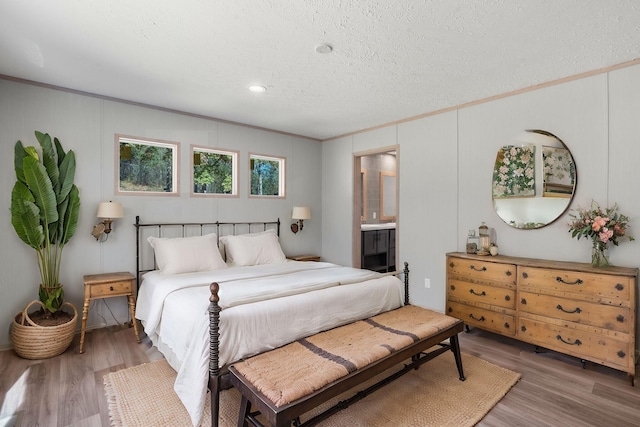 bedroom featuring a textured ceiling, connected bathroom, hardwood / wood-style flooring, and ornamental molding