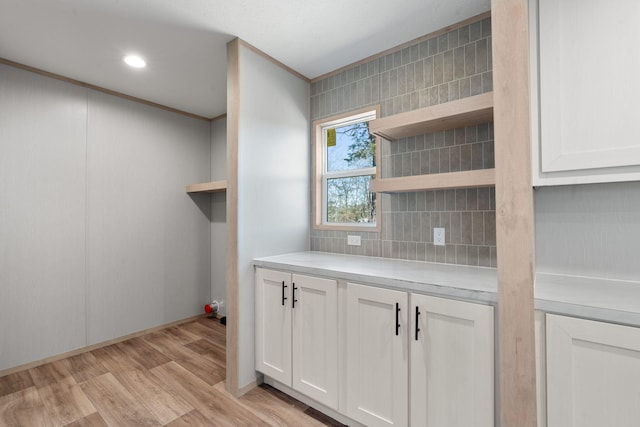 kitchen with white cabinets, light wood-type flooring, crown molding, and backsplash