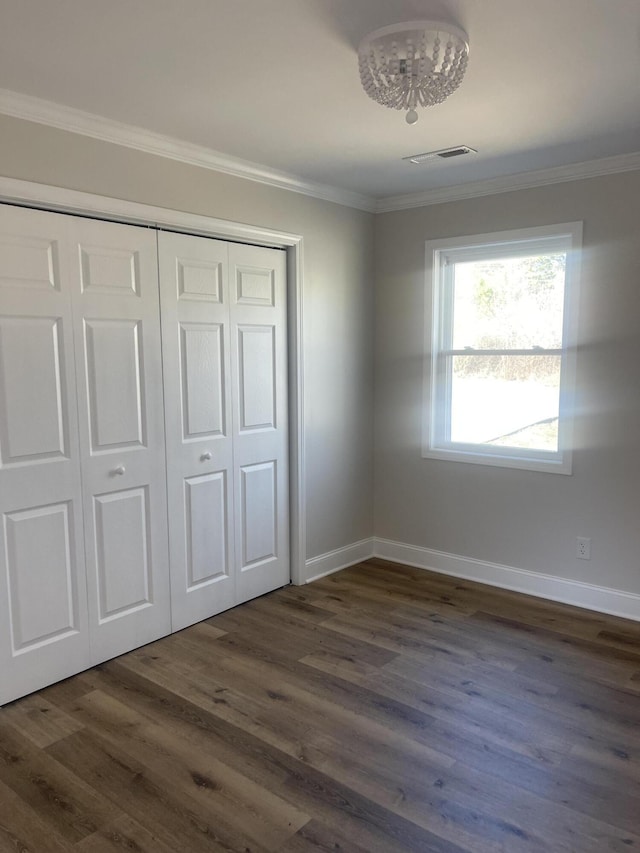 unfurnished bedroom featuring visible vents, baseboards, dark wood finished floors, ornamental molding, and a closet