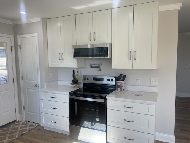 kitchen featuring wood finished floors, baseboards, ornamental molding, stainless steel appliances, and white cabinets