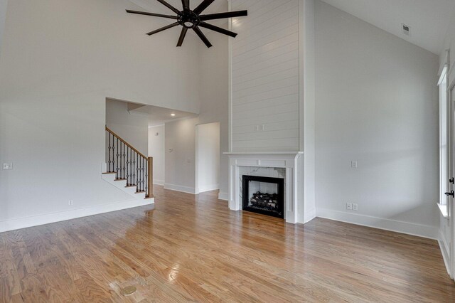 unfurnished living room featuring a high end fireplace, light wood-type flooring, high vaulted ceiling, and ceiling fan