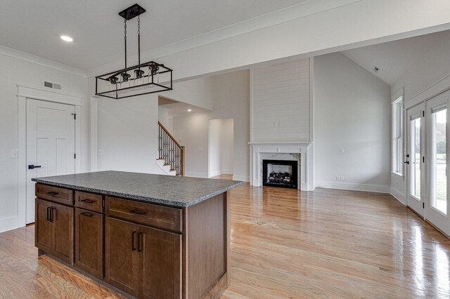 kitchen featuring a high end fireplace, light wood-type flooring, vaulted ceiling, a kitchen island, and hanging light fixtures