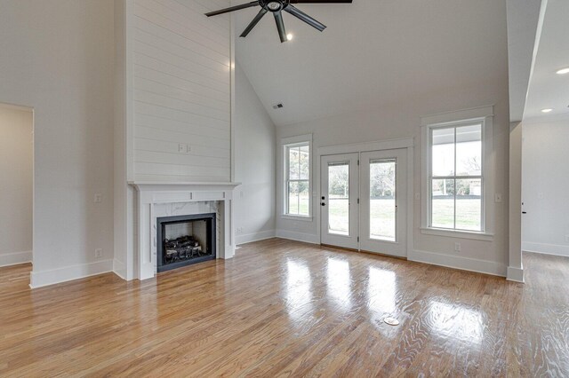 unfurnished living room featuring light hardwood / wood-style floors, high vaulted ceiling, ceiling fan, and a premium fireplace