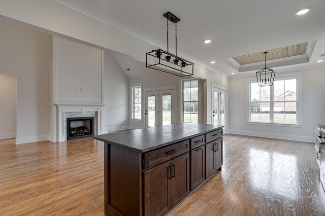 kitchen with french doors, light wood-type flooring, a tray ceiling, a kitchen island, and hanging light fixtures