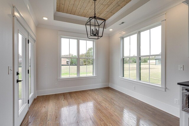 unfurnished dining area featuring a raised ceiling, plenty of natural light, hardwood / wood-style floors, and a notable chandelier