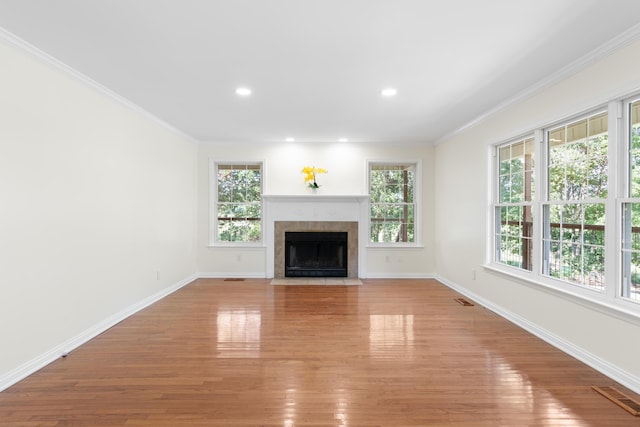 unfurnished living room featuring a tiled fireplace, light hardwood / wood-style floors, and ornamental molding