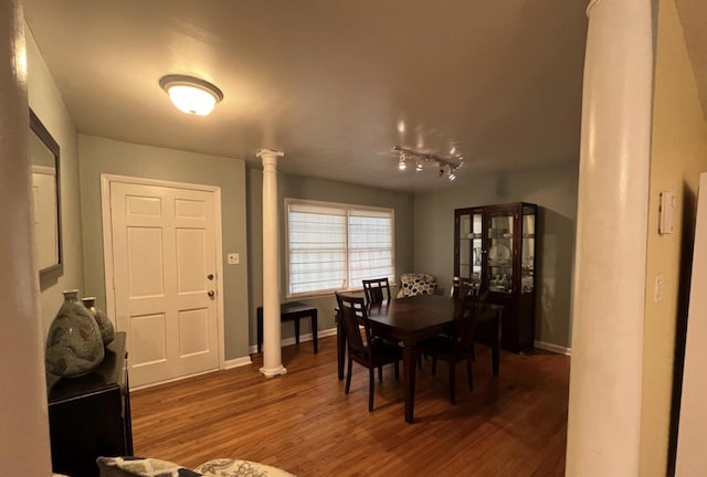 dining space with track lighting, dark wood-type flooring, and decorative columns