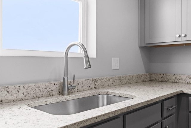 room details featuring light stone counters, gray cabinets, and sink