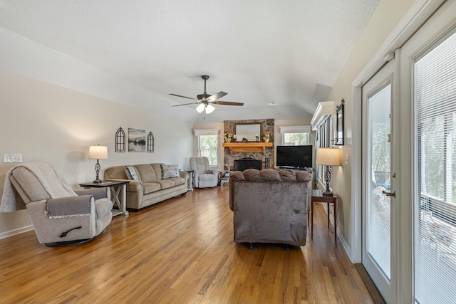 living room with a ceiling fan, a fireplace, light wood-type flooring, lofted ceiling, and baseboards