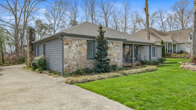 view of side of home featuring concrete driveway, stone siding, a shingled roof, a yard, and a chimney