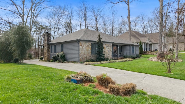view of side of property featuring stone siding, driveway, a yard, and a chimney