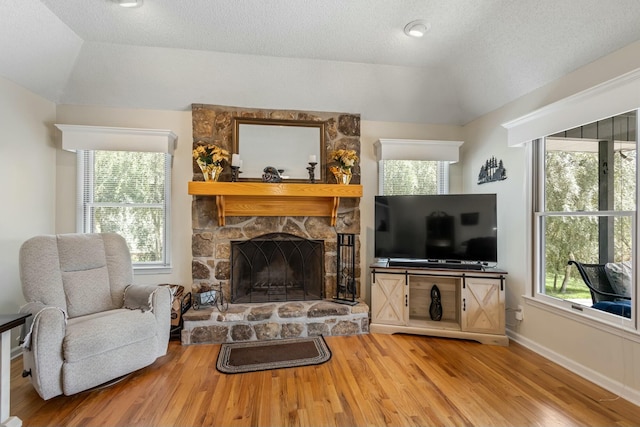 living area featuring a textured ceiling, a healthy amount of sunlight, a fireplace, and wood finished floors