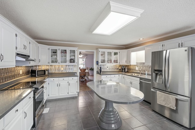 kitchen with stainless steel appliances, under cabinet range hood, a sink, white cabinets, and glass insert cabinets