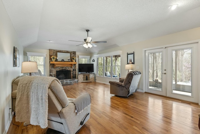 living area with lofted ceiling, light wood-style floors, visible vents, a ceiling fan, and a stone fireplace